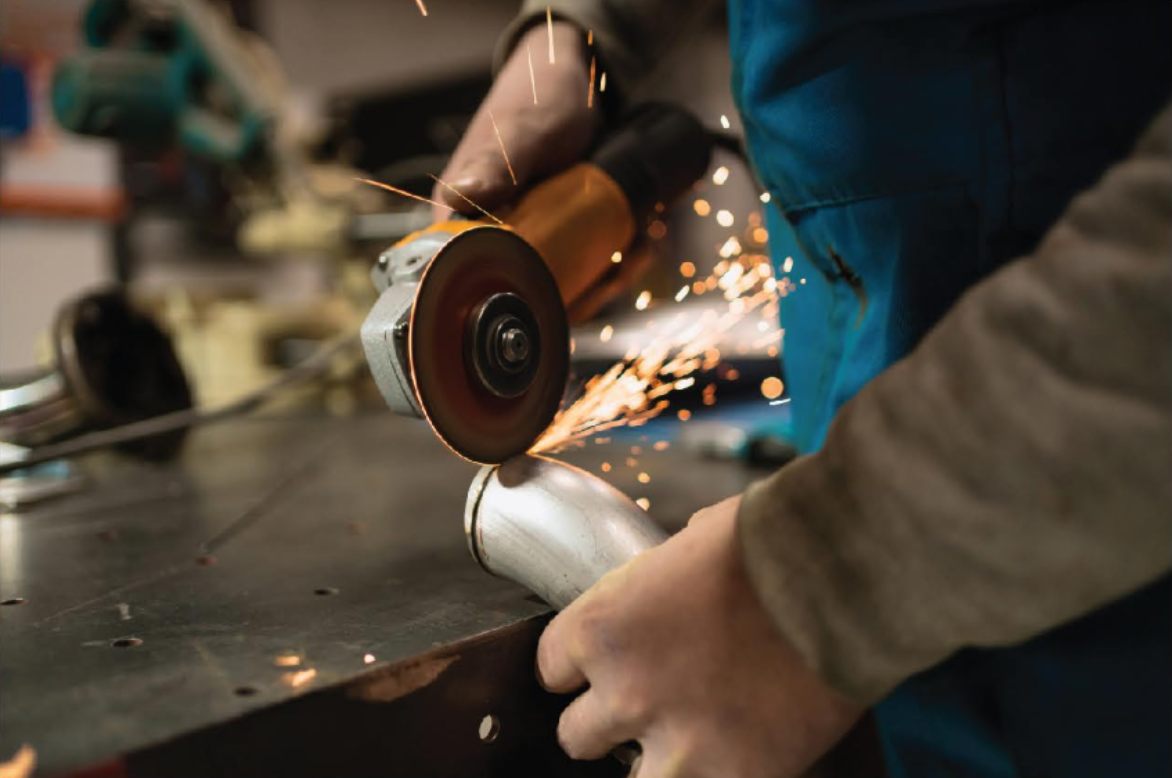 A worker grinding a steel pipe with an angle grinder